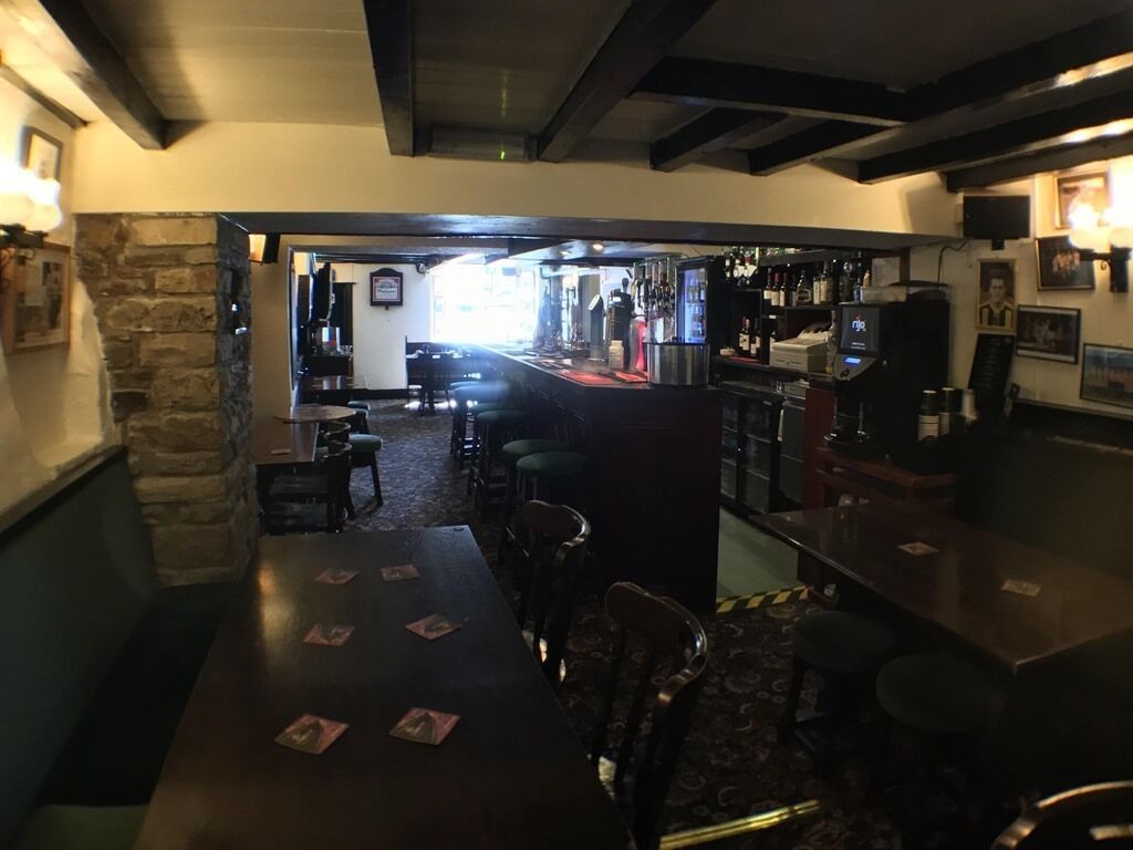 A bar area with a stone wall, wooden ceiling beams, and a bar counter with stools.