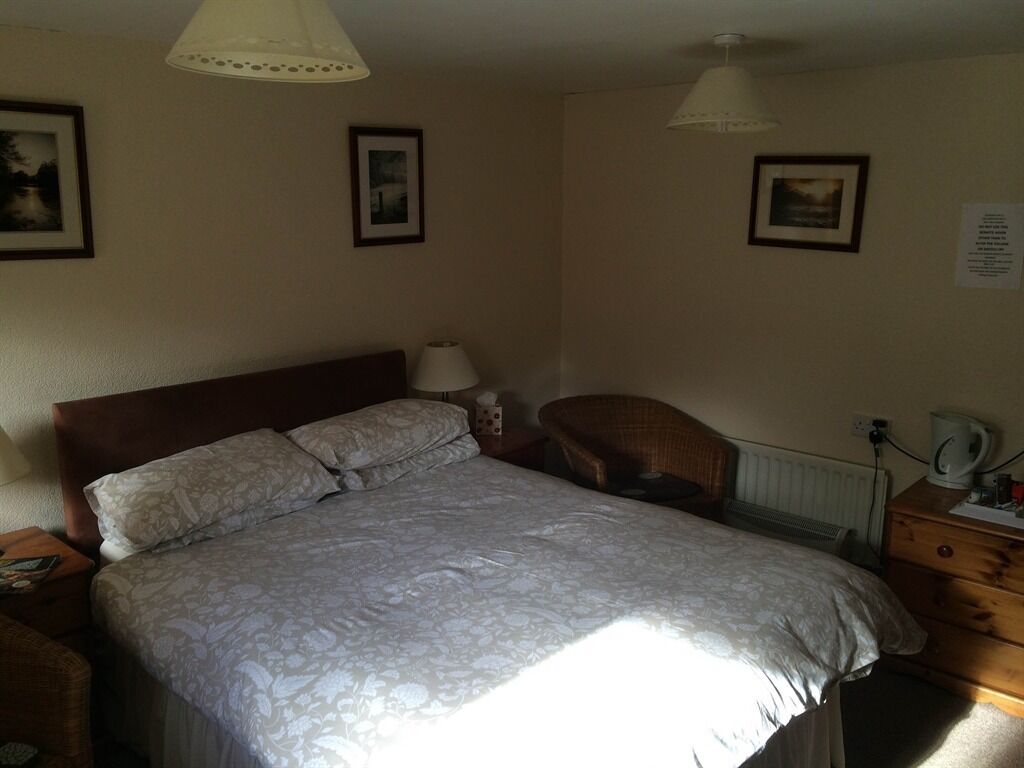 Een slaapkamer met een groot bed, twee bedlampjes, een stoel, een dressoir en lijstjes met foto’s aan de muur.