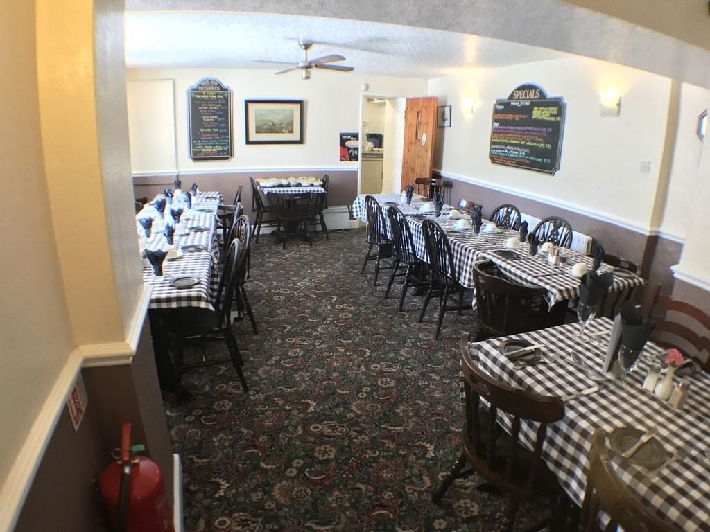 A dining area with checkered tablecloths, multiple tables, and chairs. There are wall signs and a ceiling fan.