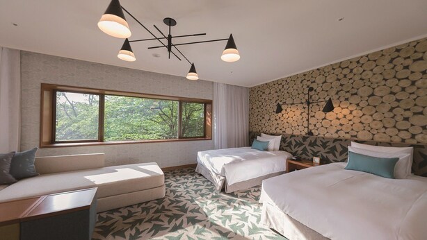 Quarto de hotel com duas camas, um sofá, uma janela grande e um lustre.