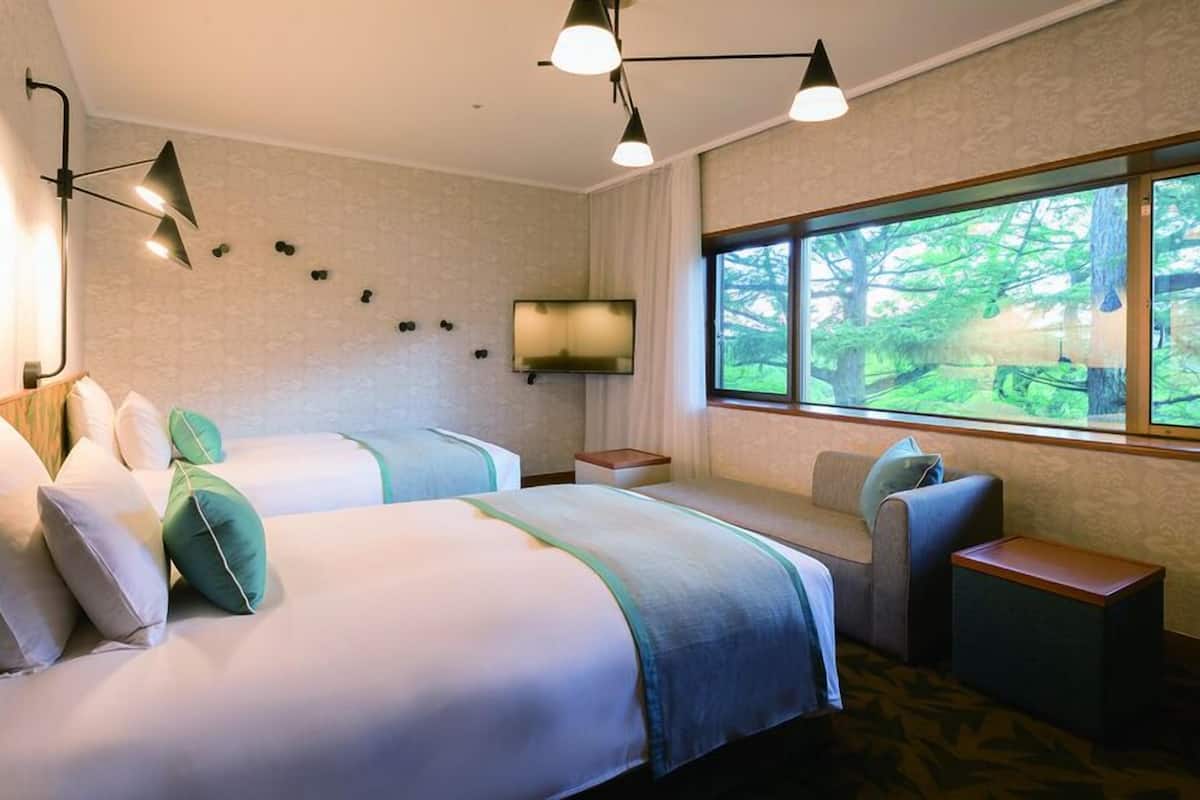 Une chambre d’hôtel avec deux lits, une télévision, une fenêtre donnant sur la forêt et un petit coin salon.
