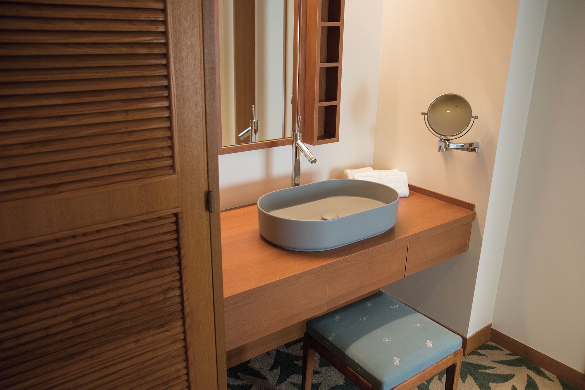 A bathroom with a wooden vanity, a round mirror, and a blue sink.