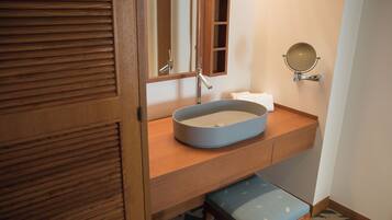 A bathroom with a wooden vanity, a round mirror, and a blue sink.