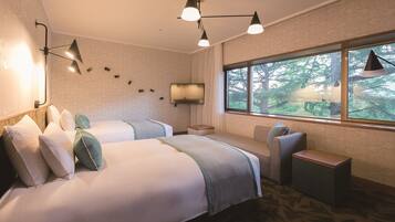 Habitación de hotel con dos camas, televisión, ventana con vista al bosque y escritorio.