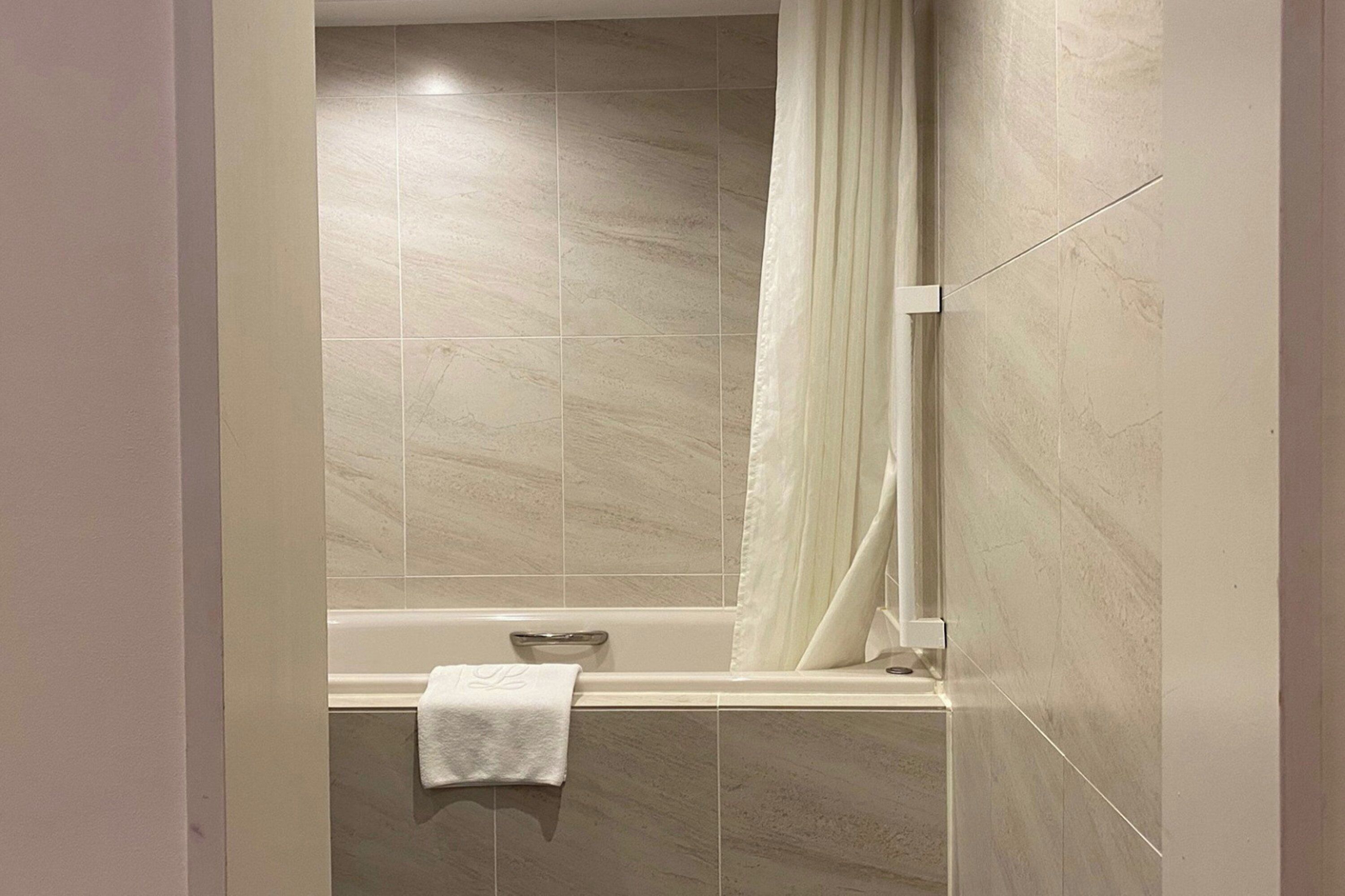 A bathroom with a bathtub, a shower curtain, and a towel hanging on the wall.