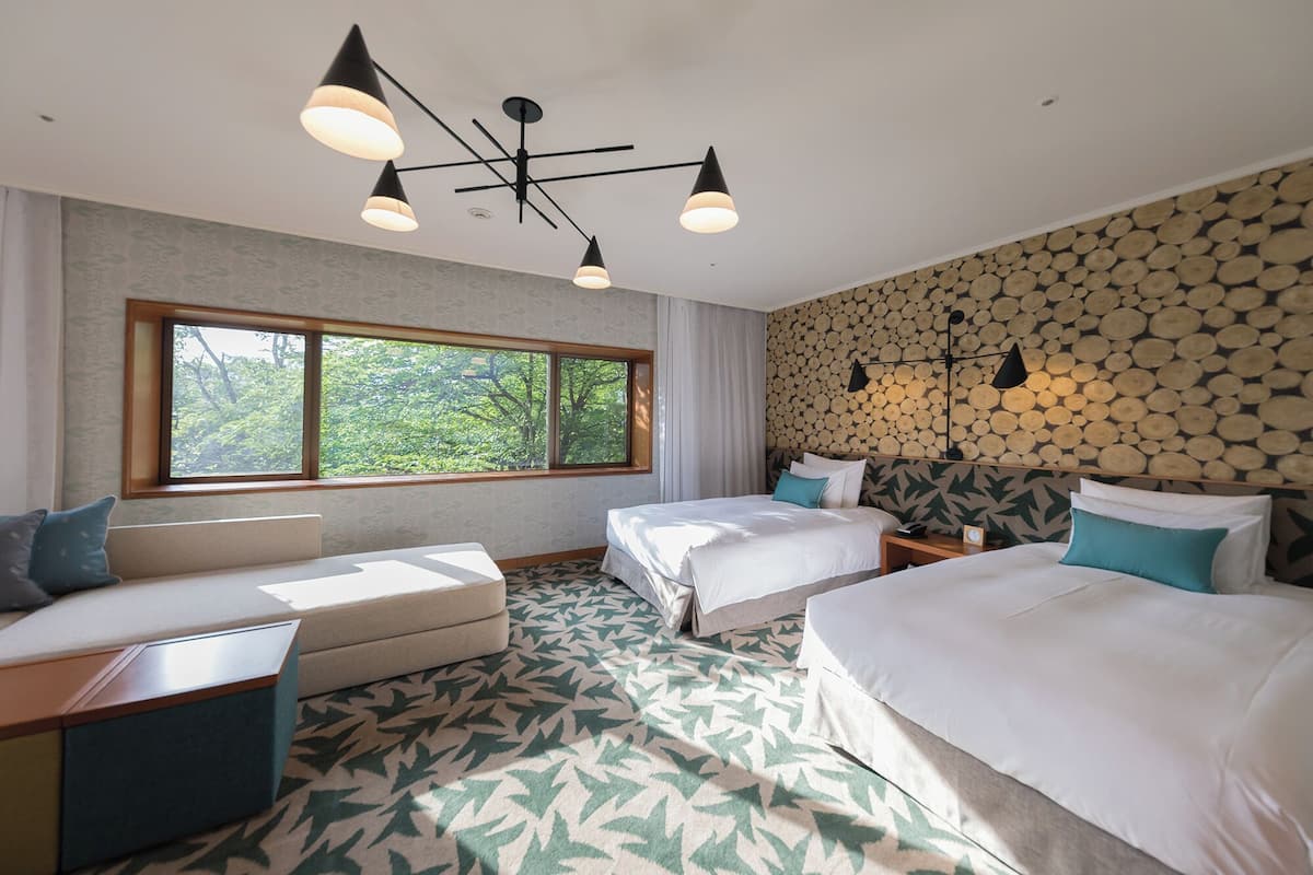 Une chambre d’hôtel avec deux lits, un canapé, une grande fenêtre et un luminaire au plafond.