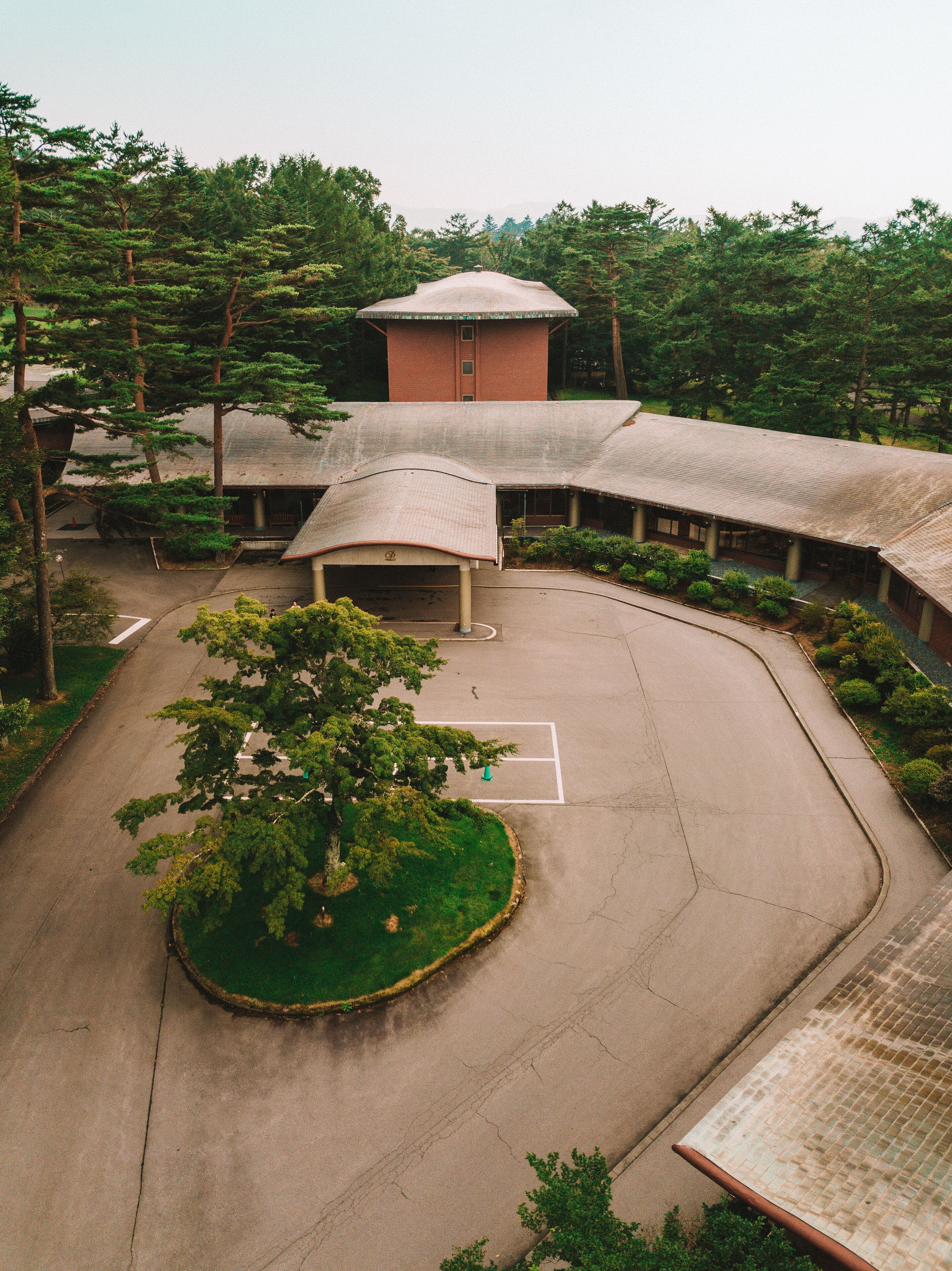 A building with a curved roof, surrounded by trees and a parking area.