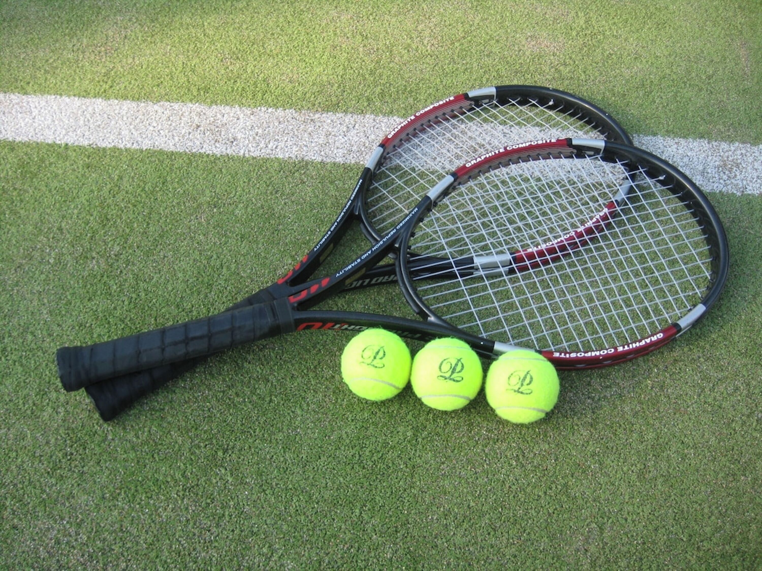 Two tennis rackets and three tennis balls on a green surface with white lines.