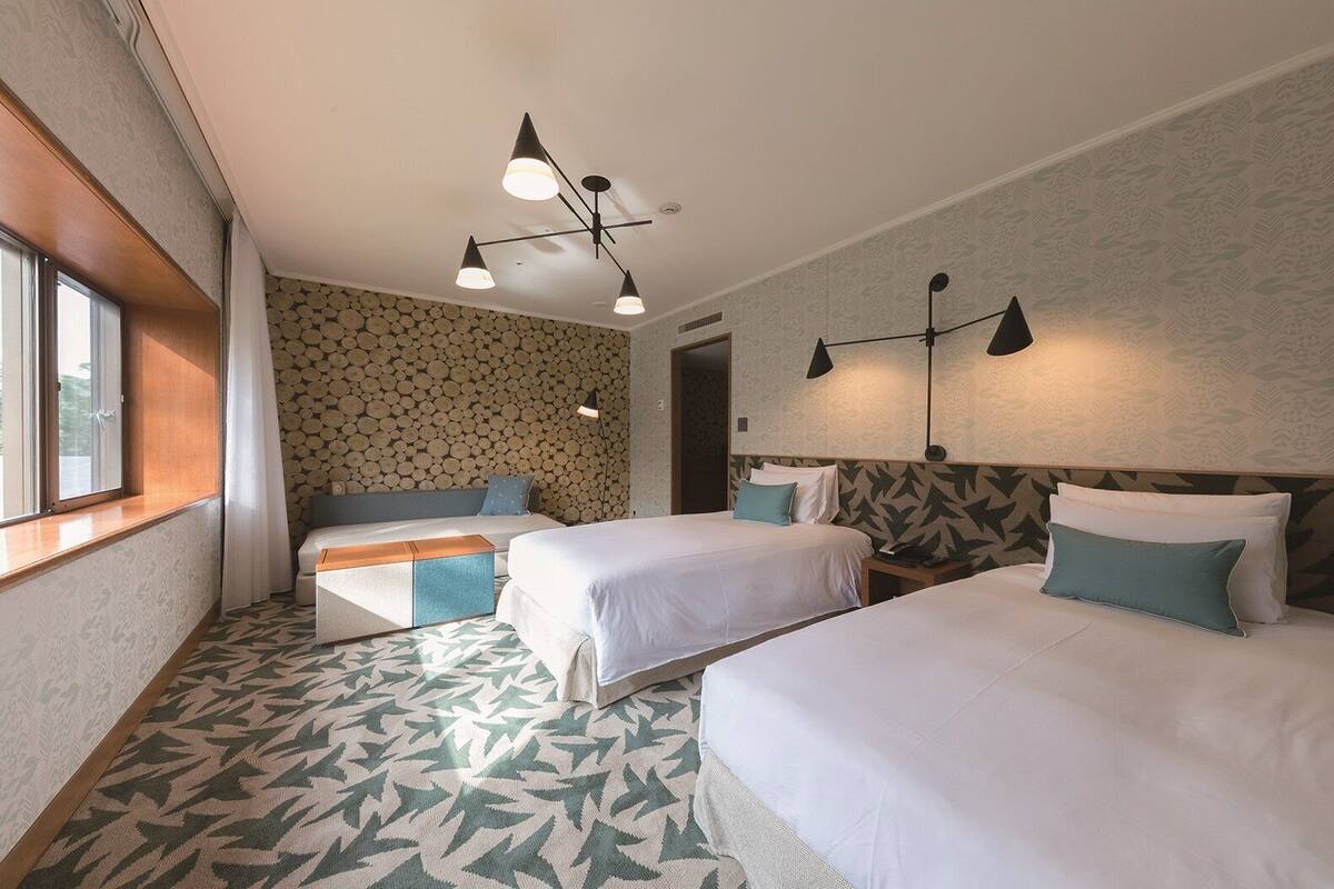 Une chambre d’hôtel avec deux lits, un coin salon et un mur décoré de motifs.