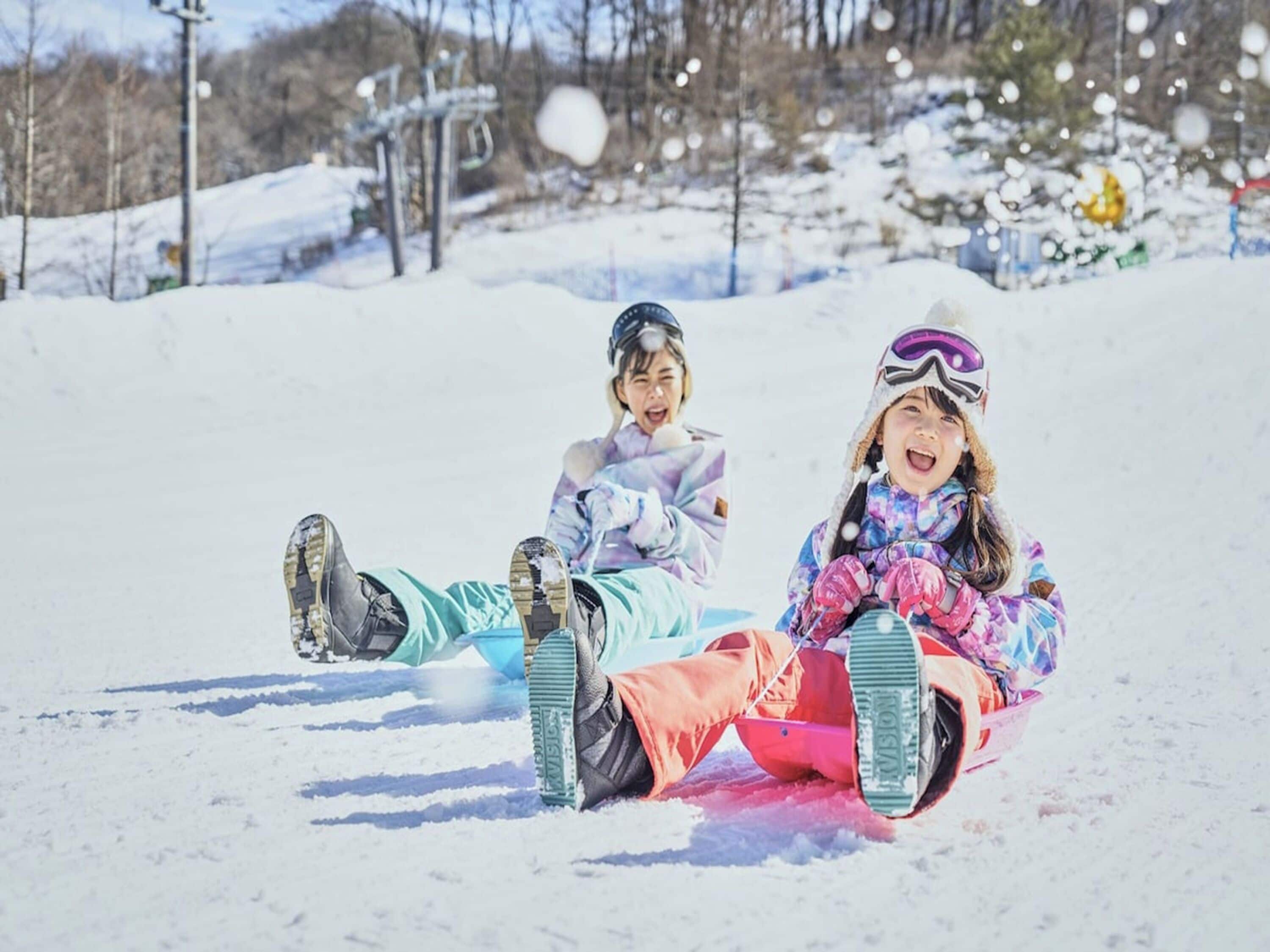 Two children sledding on a snowy slope.