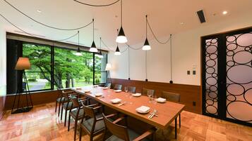 A conference room with a long table set for a meeting, large windows with a view of trees, and a decorative screen on the right.