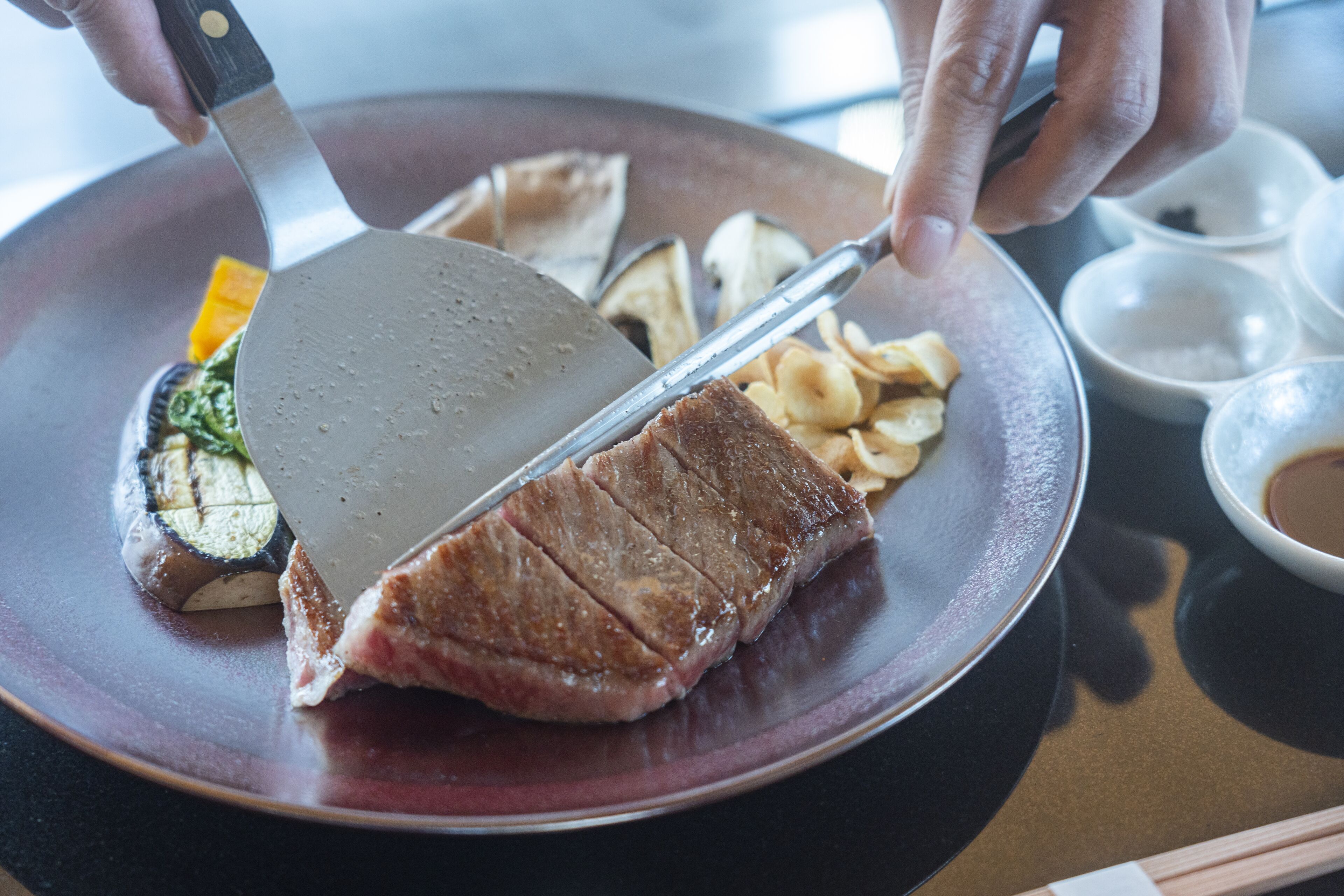 Una persona che taglia una bistecca su un piatto con una spatola.