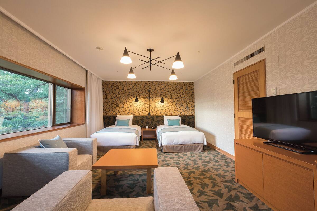Une chambre d’hôtel avec deux lits, une télévision, un canapé, une table et une grande fenêtre.