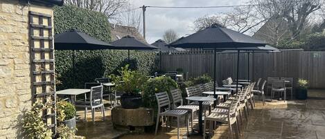 An outdoor patio with tables and chairs, surrounded by a wooden fence and potted plants.