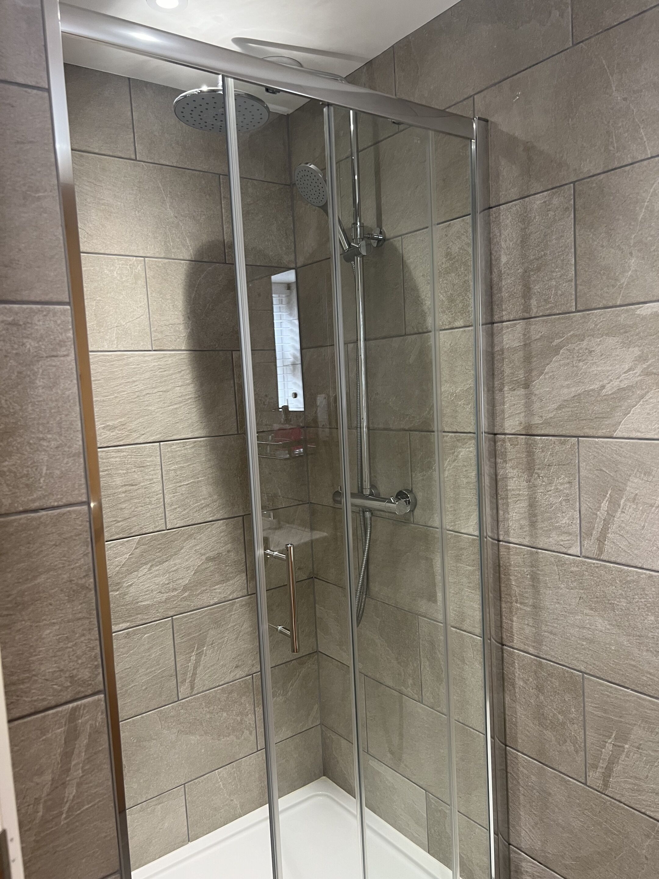 A glass-enclosed shower stall with a handheld showerhead and a wall-mounted faucet.