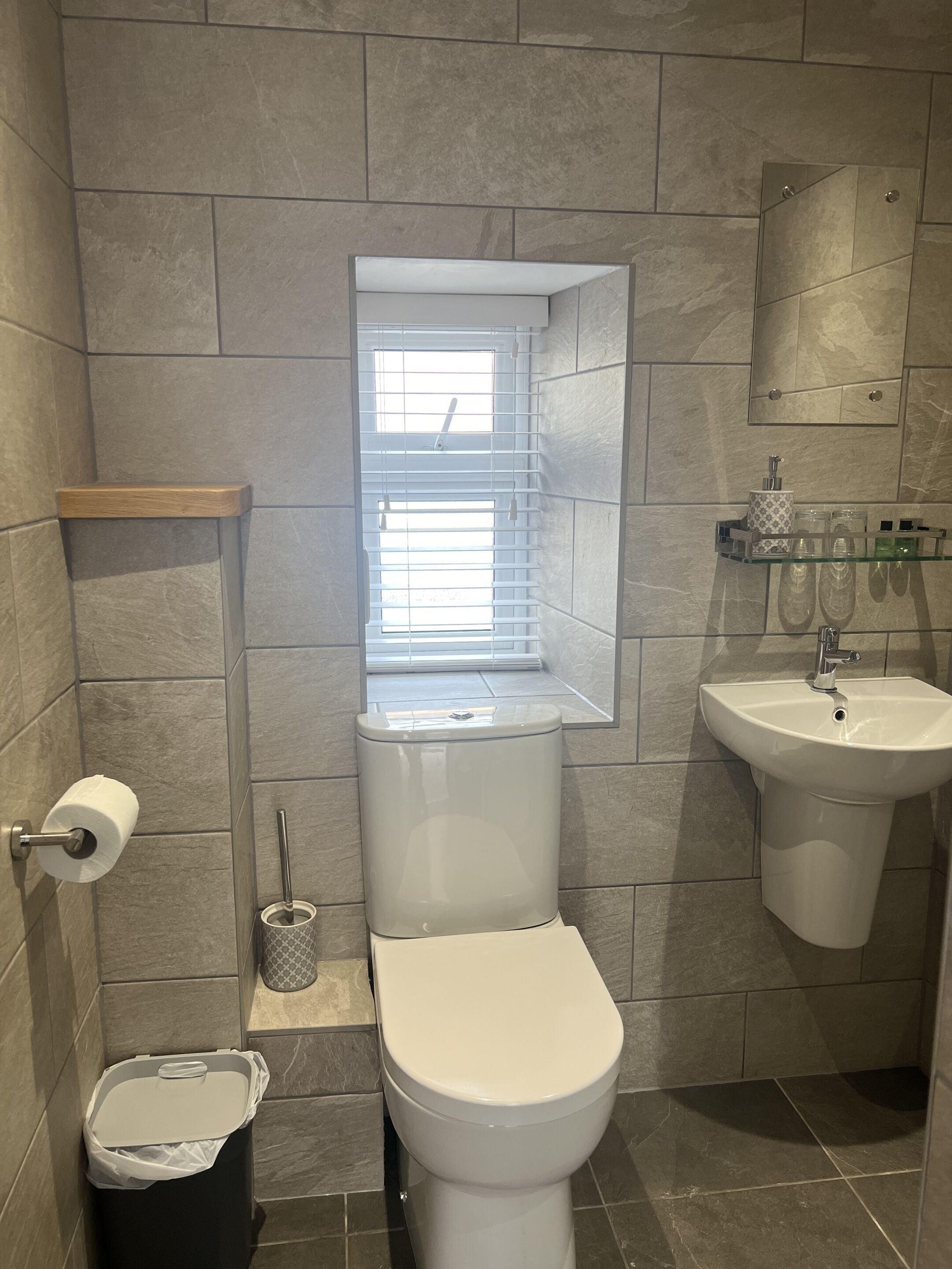 A bathroom with a toilet, bidet, sink, and a window with blinds.