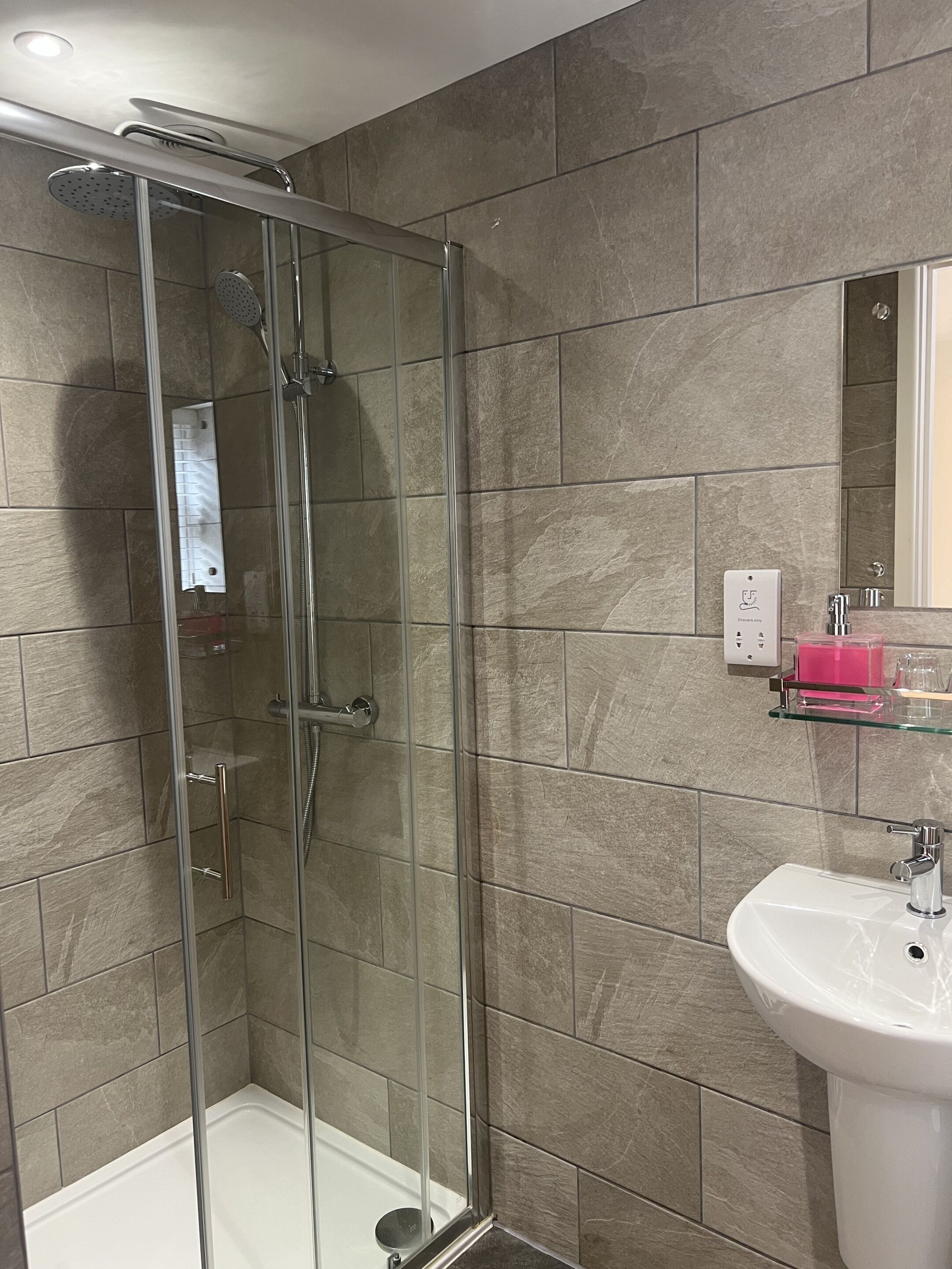 Une salle de bain moderne avec une douche en verre, un lavabo blanc et un miroir au-dessus du lavabo.