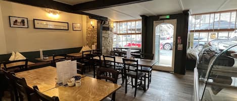 Un interior de restaurante con mesas y sillas de madera, cuadros en las paredes y una pared decorativa de piedra.