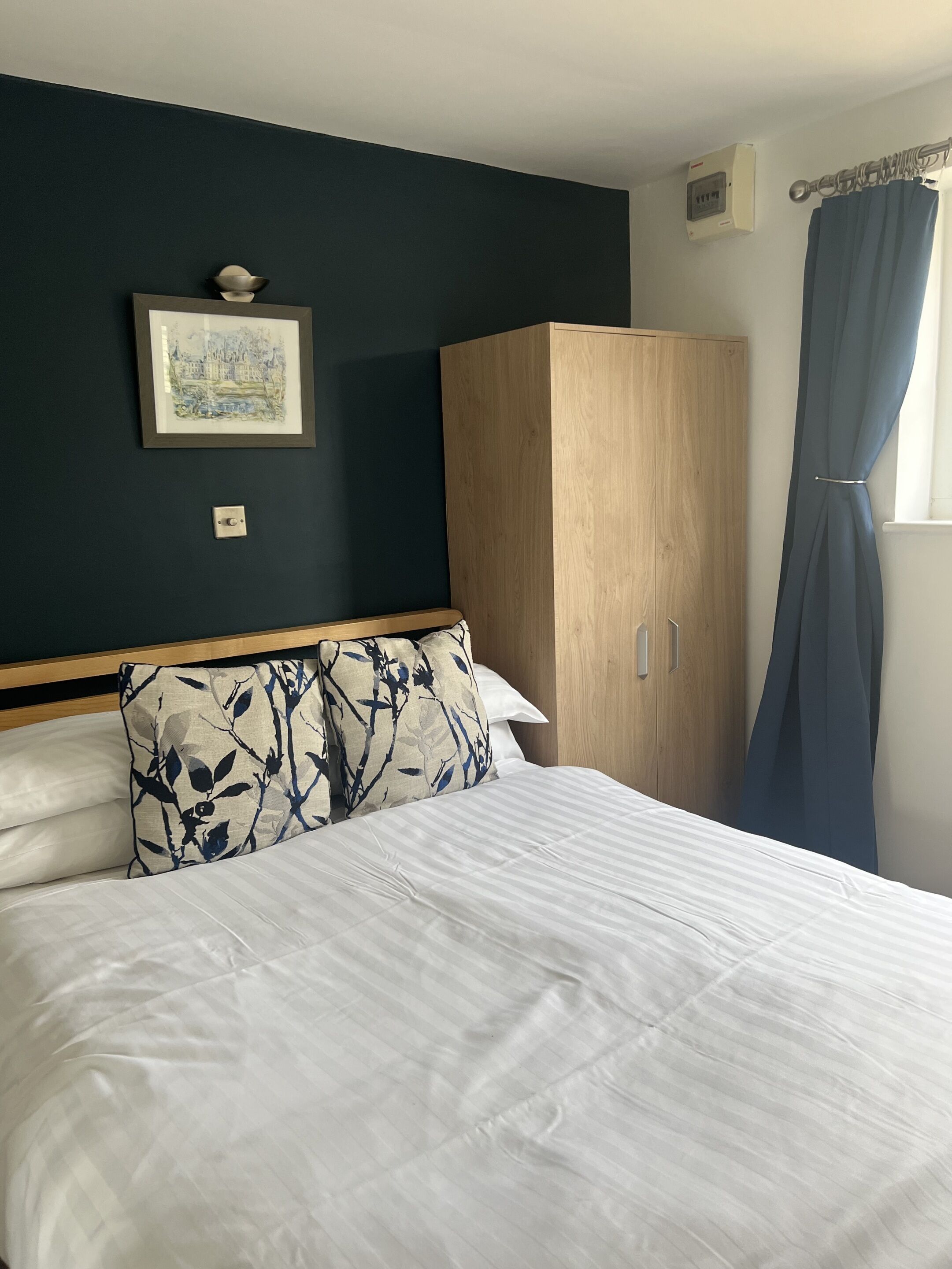 Quarto com uma cama, um guarda-roupa de madeira, um quadro na parede e uma janela com cortinas.