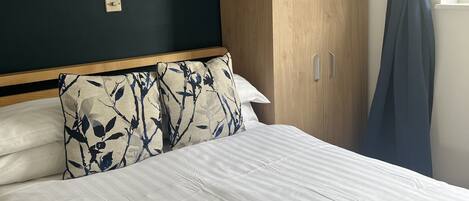 Quarto com uma cama, um guarda-roupa de madeira, um quadro na parede e uma janela com cortinas.