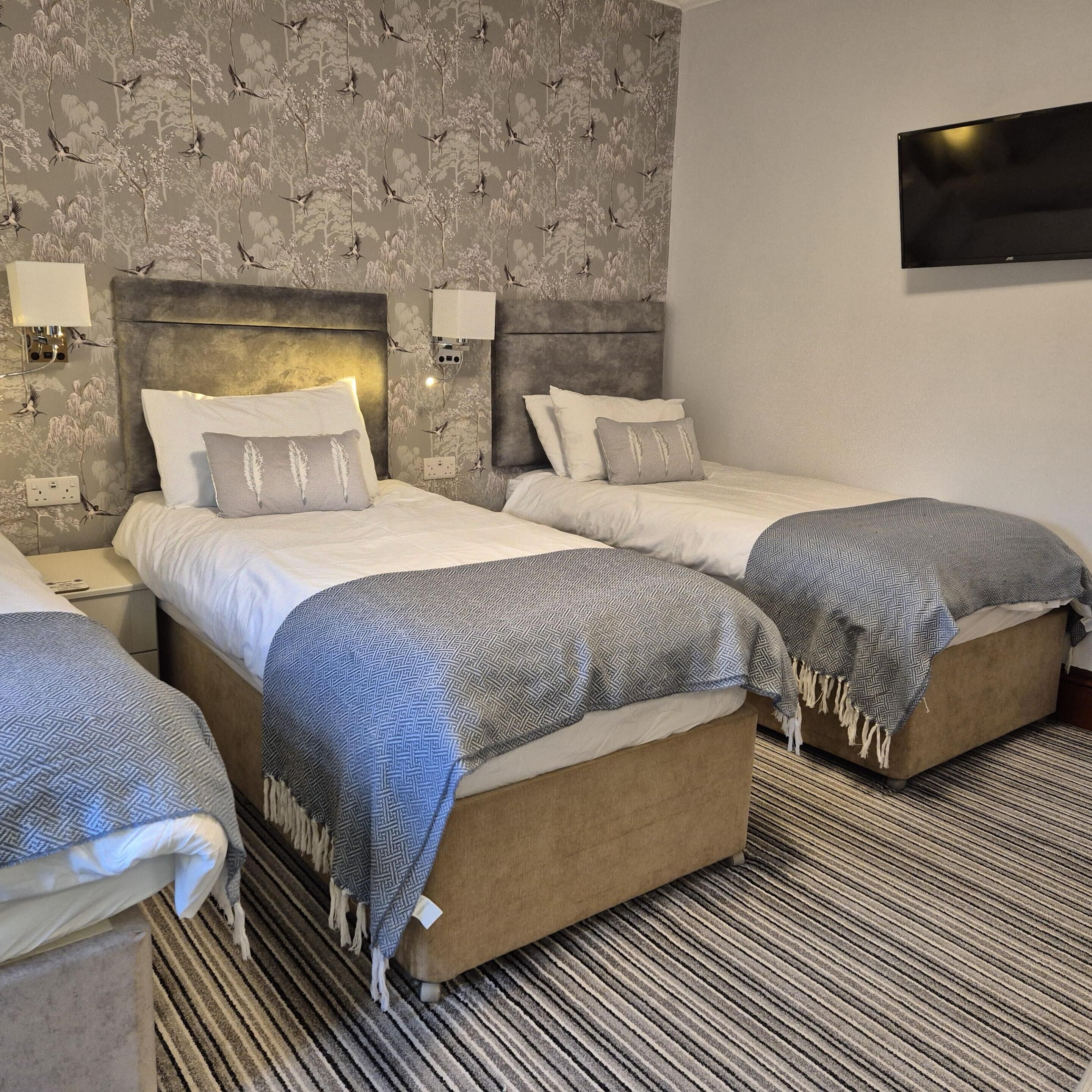A hotel room with two beds, a large flat-screen TV, and a patterned wallpaper.
