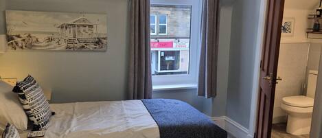 A hotel room with two beds, a window with curtains, a painting on the wall, and a view of the street outside.