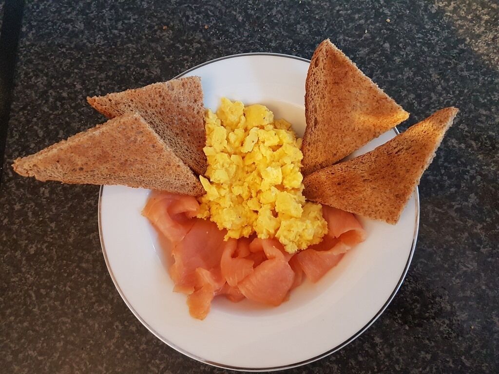 Un plato con huevos revueltos, salmón ahumado y tostadas triangulares.
