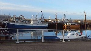 Ein Hafen mit einem großen blauen Schiff, kleineren Booten und einem weißen Gebäude im Hintergrund.