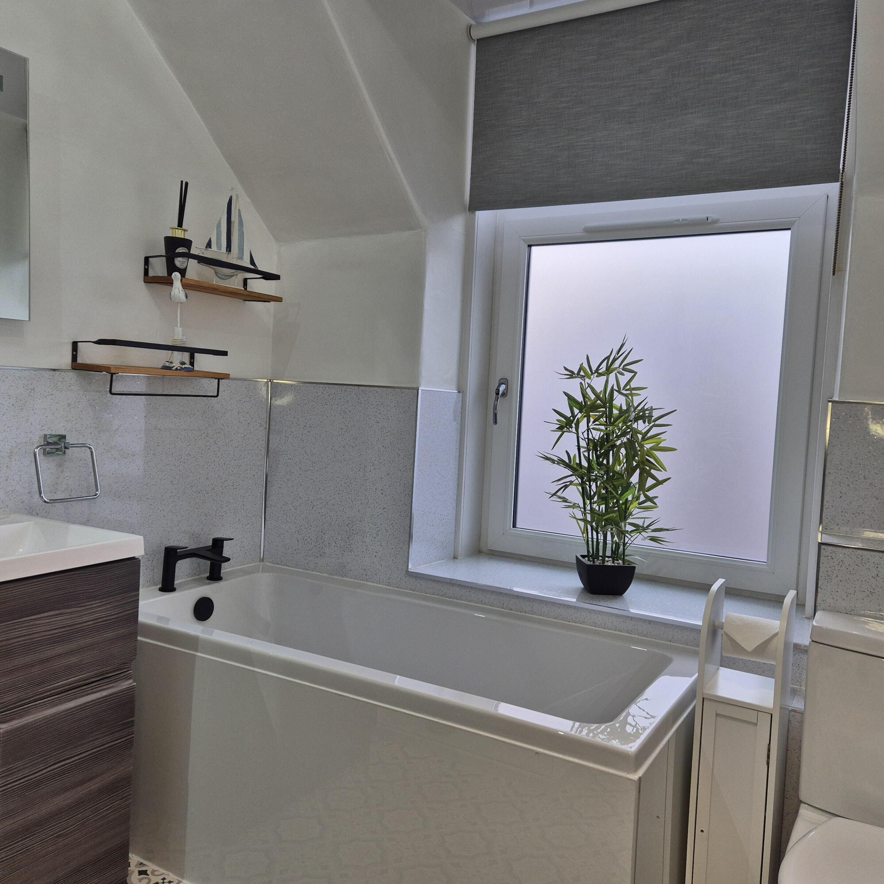 A modern bathroom with a bathtub, a window with a view, and a potted plant on the windowsill.
