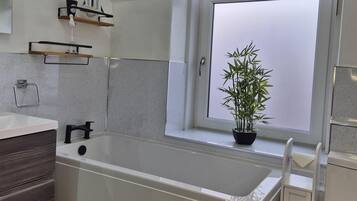 A modern bathroom with a bathtub, a window with a view, and a potted plant on the windowsill.