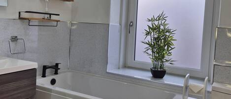 A modern bathroom with a bathtub, a window with a view, and a potted plant on the windowsill.
