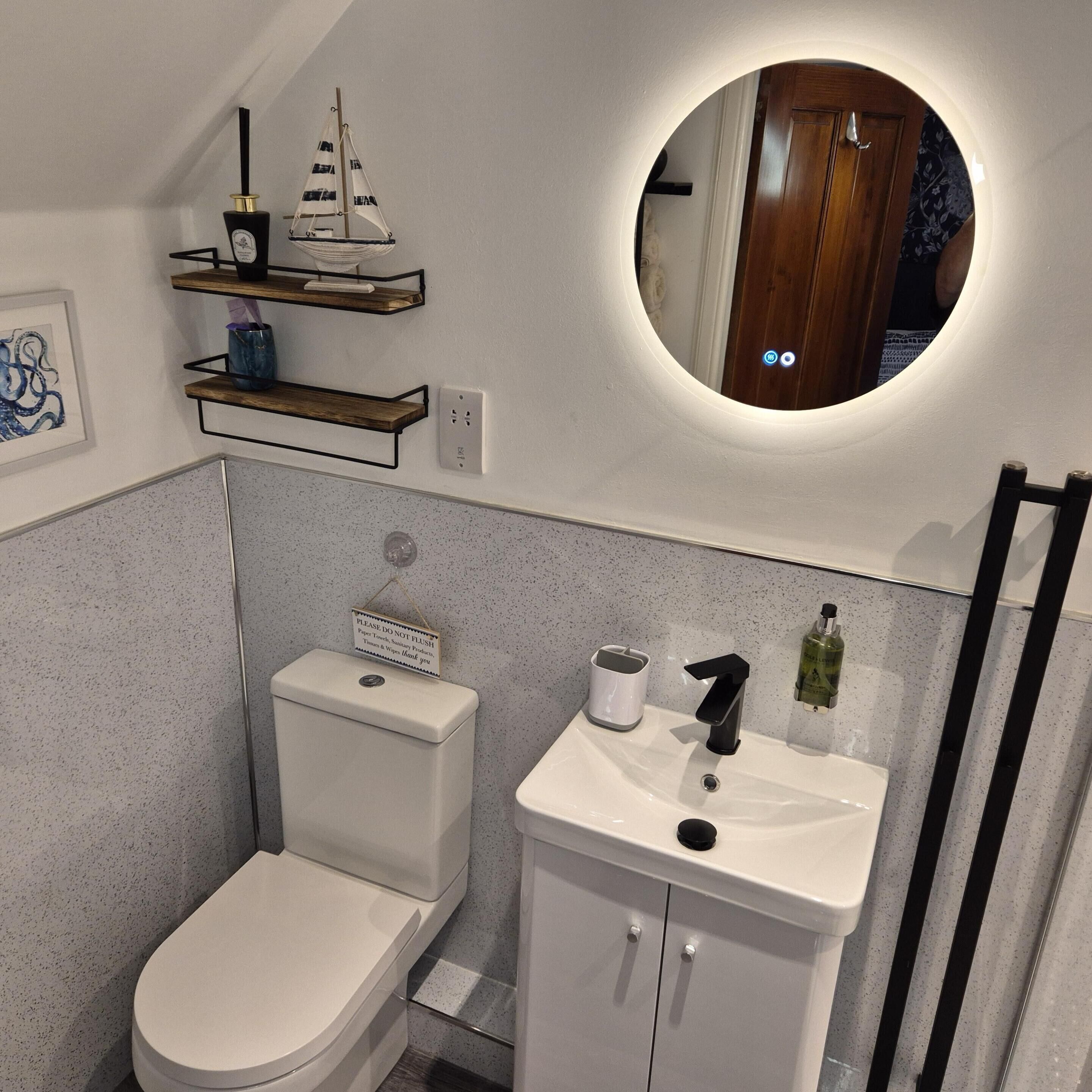 A modern bathroom with a toilet, sink, and a small shelf above the toilet.