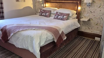 Une chambre d’hôtel avec un grand lit, deux lampes fixées au mur, un papier peint à motifs floraux et un tableau accroché au mur.