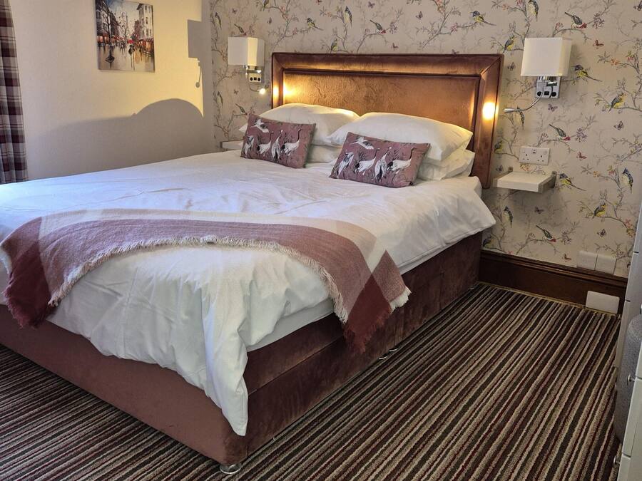Une chambre d’hôtel avec un grand lit, deux lampes fixées au mur, un papier peint à motifs floraux et un tableau accroché au mur.