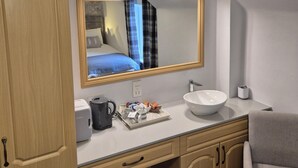 Ein Hotelbad mit einem großen Spiegel, einem Waschbecken, einem Schrank und einem im Spiegel sichtbaren Bett.