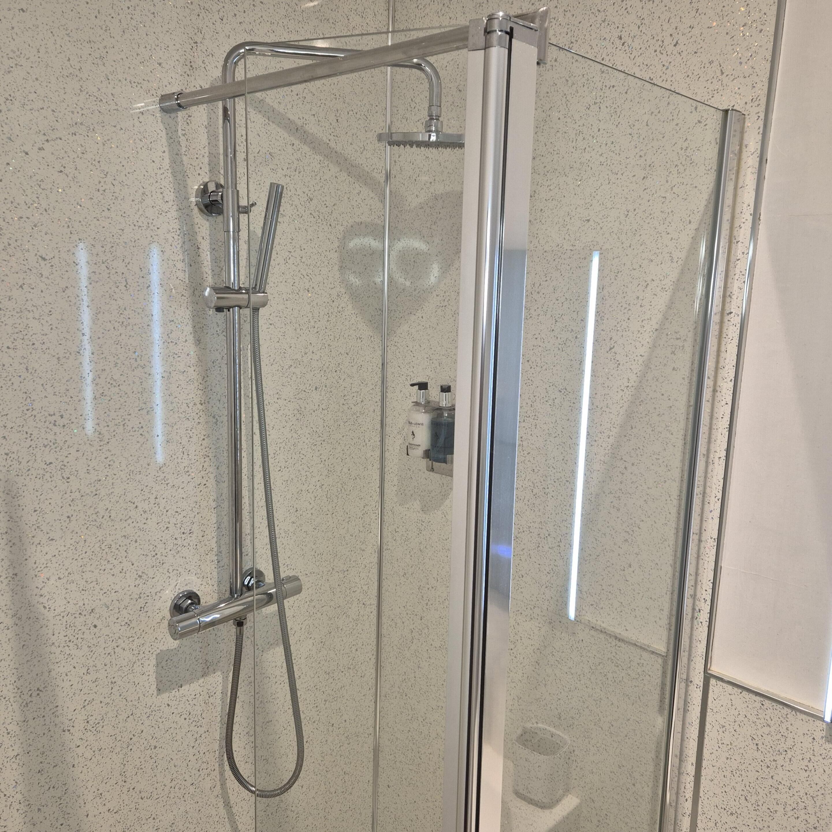 Een douchecabine met glazen wanden, een handdouche en een aparte douchestraal.
