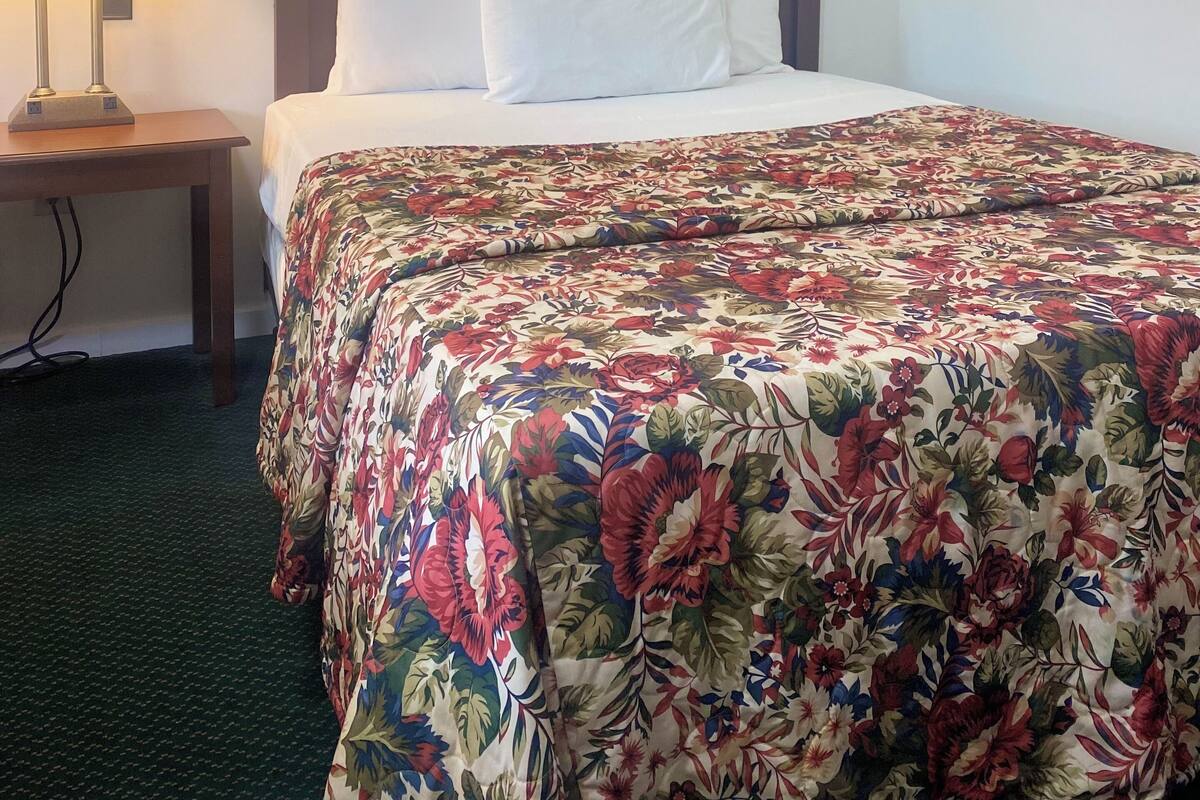 Una habitación de hotel con una cama, una mesita de noche con lámpara y una colcha estampada con motivos florales.