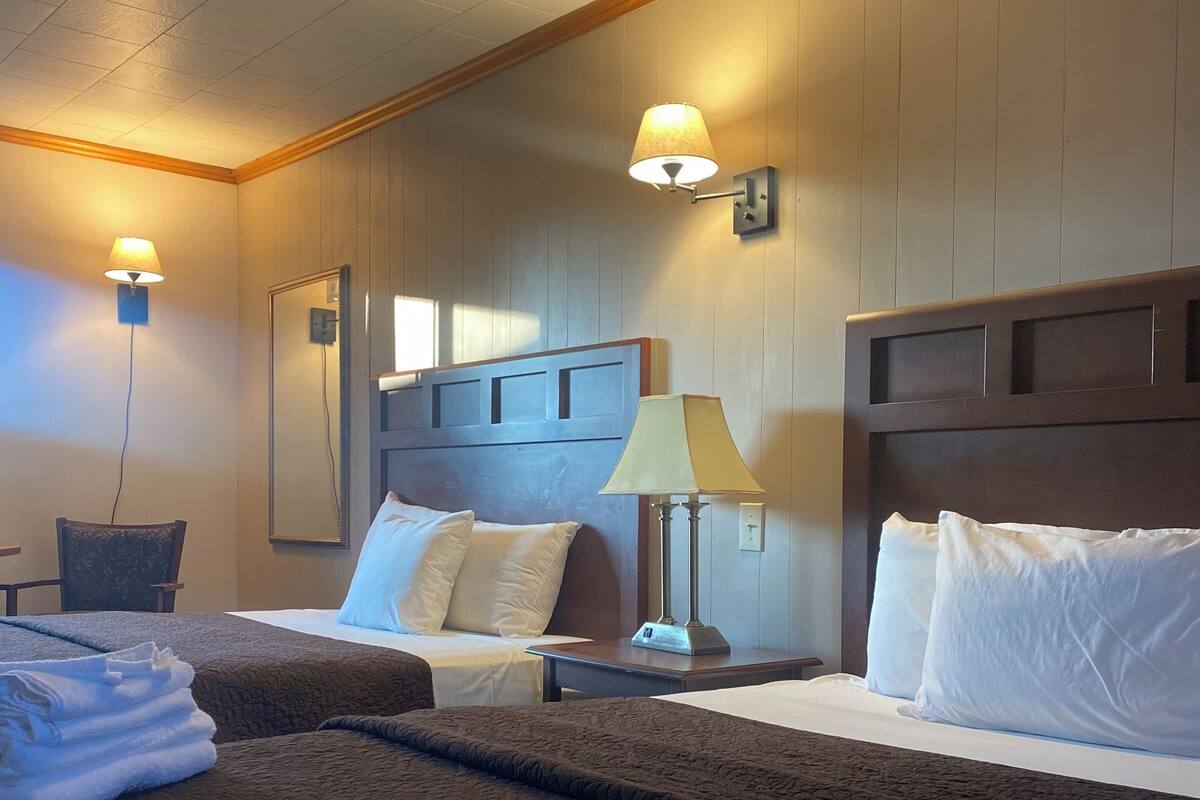 Habitación de hotel con dos camas, una mesita de noche, una lámpara y un espejo.