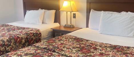 A hotel room with two beds, each with a floral bedspread and white pillows. There is a nightstand with a lamp between the beds.