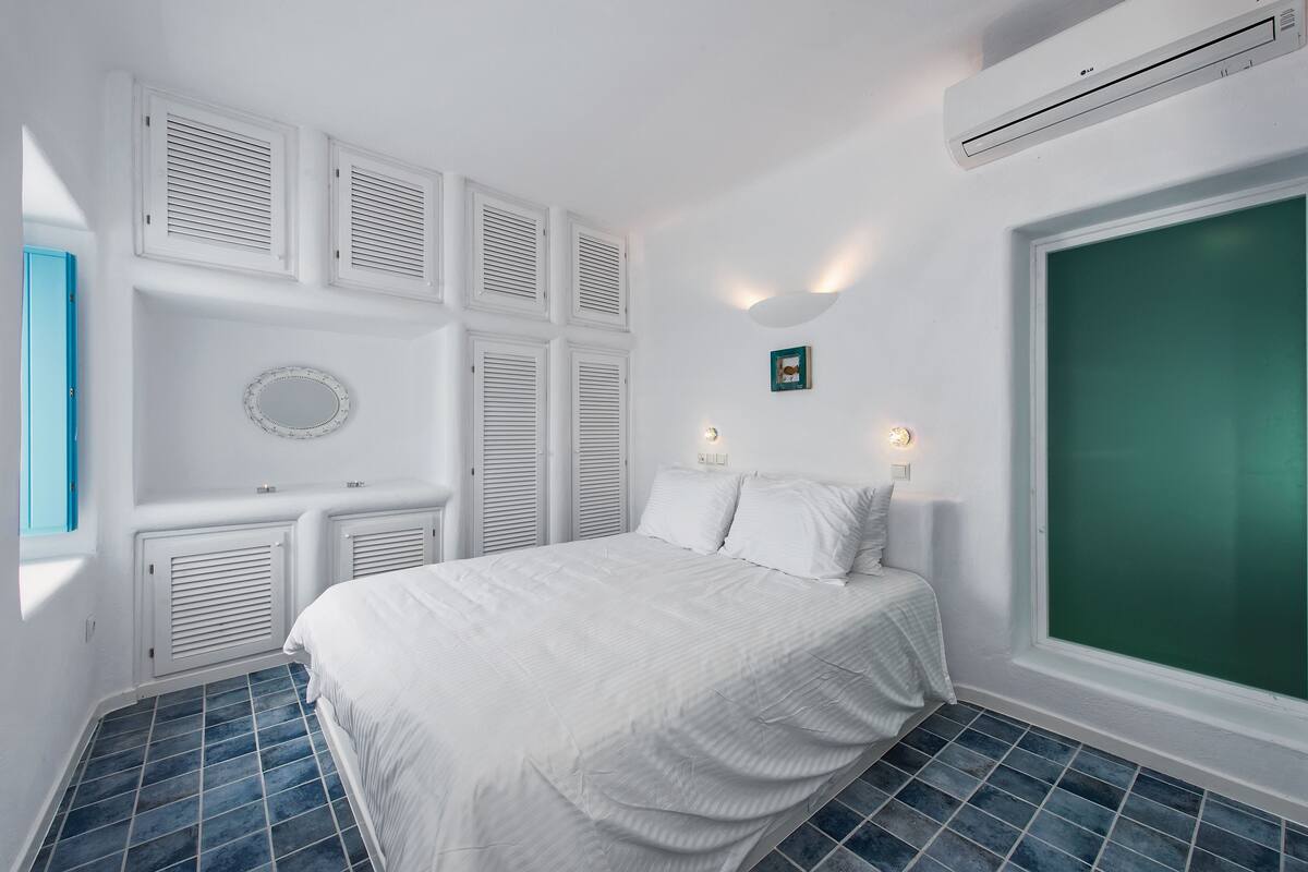 Une chambre à coucher avec un lit, des murs blancs, une grande fenêtre et une vue sur un paysage verdoyant.