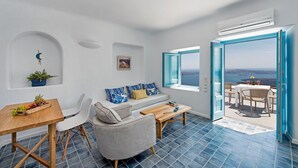 A modern living room with a sofa, coffee table, and dining table. There is a view of the sea through large windows.