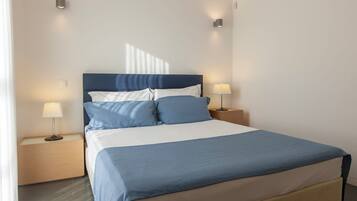 Una cama bien tendida con una colcha azul y blanca, dos mesitas de noche con lámparas y un cabecero moderno.