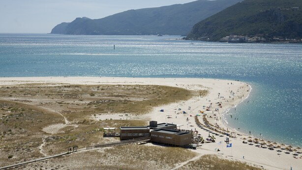 Ein Küstenstrand mit sandigem Ufer, einigen Gebäuden und freiem Blick auf das Meer.