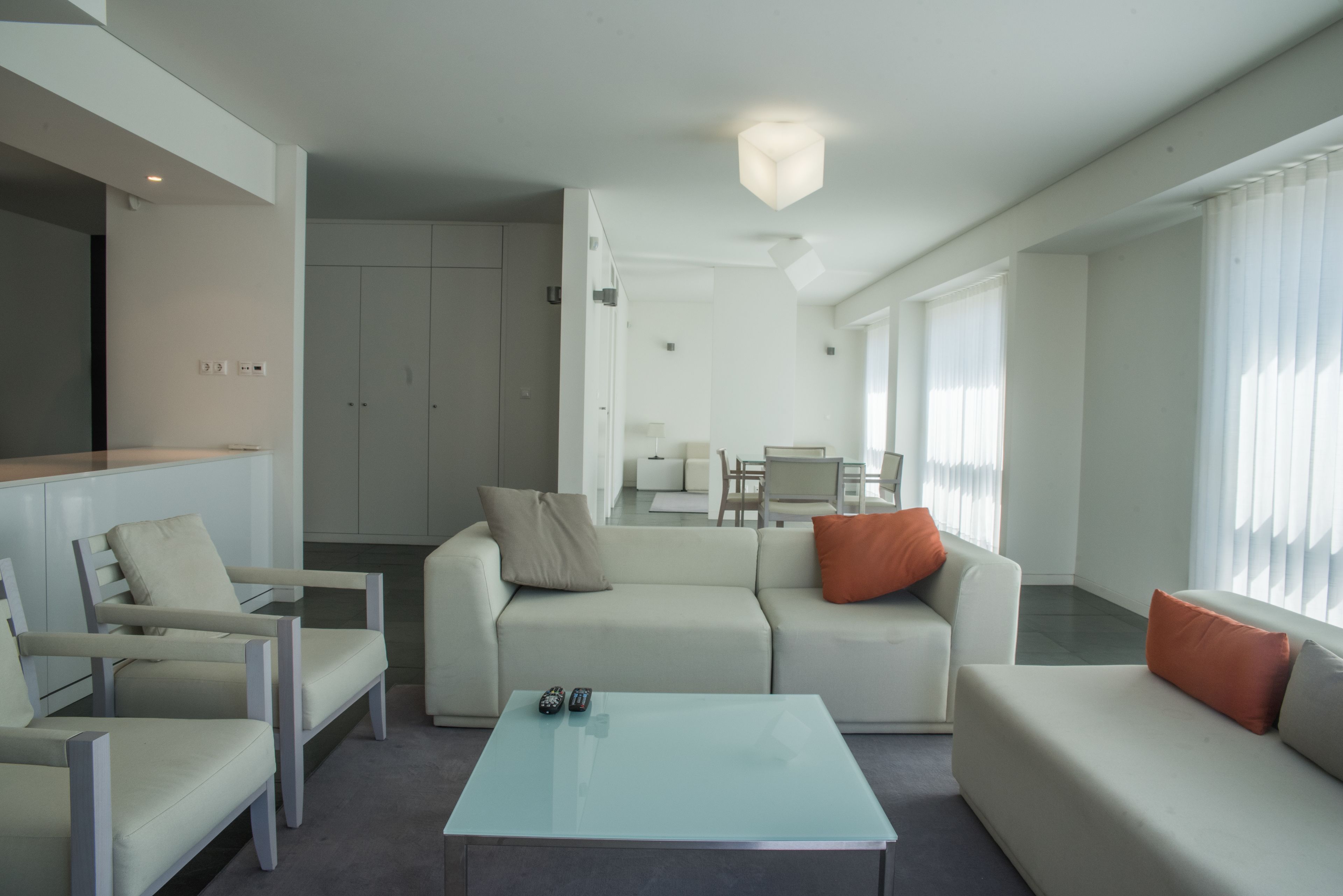 A modern living room with a glass coffee table, two sofas, and a dining area in the background.