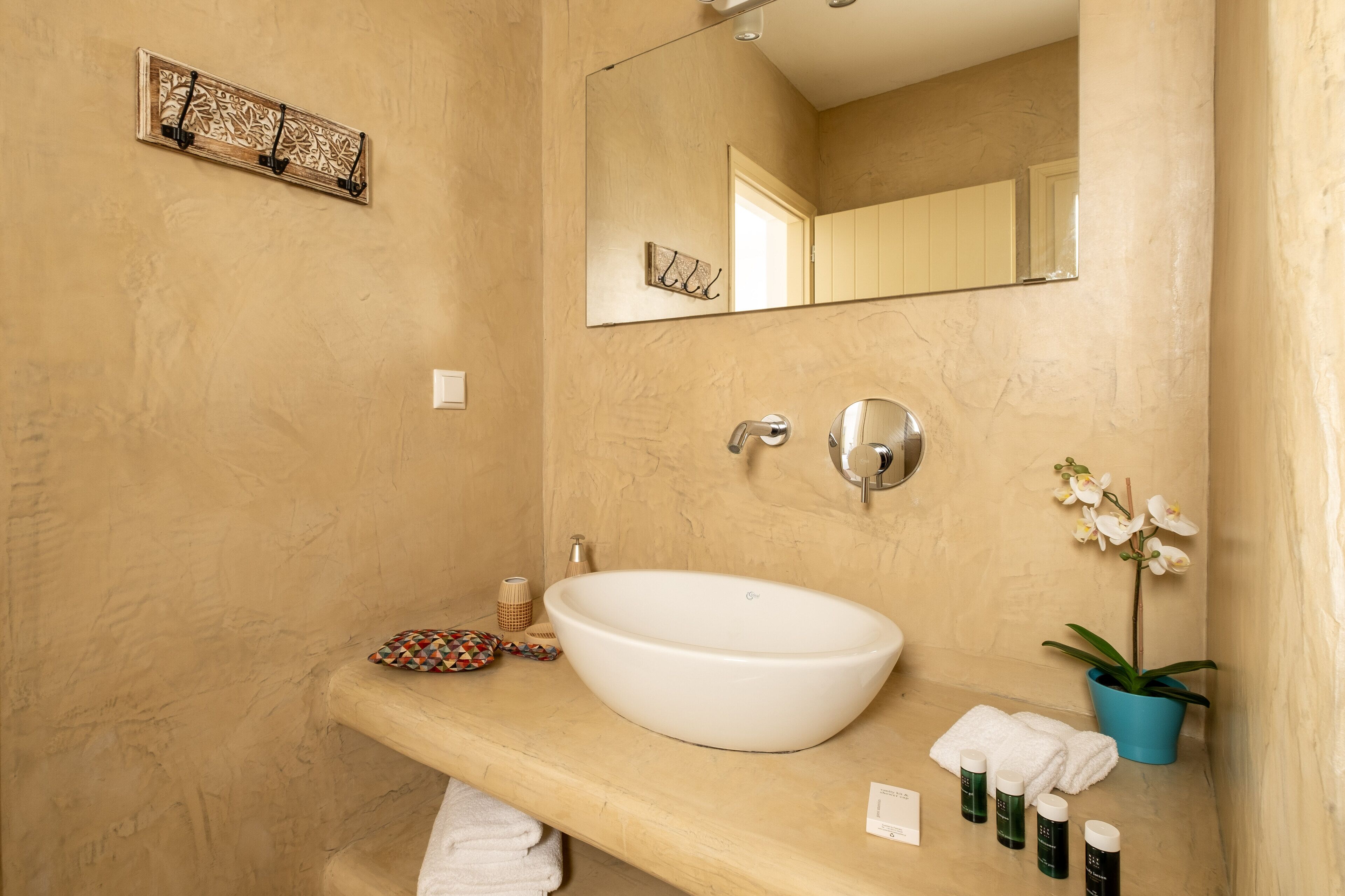 Un baño con un lavamanos grande de color blanco, un espejo, un perchero para toallas, una planta pequeña y un adorno en la pared.