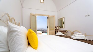A hotel room with a bed, a bathroom with a mirror, and a view of the city. - White Orchid Villa (Santorini)