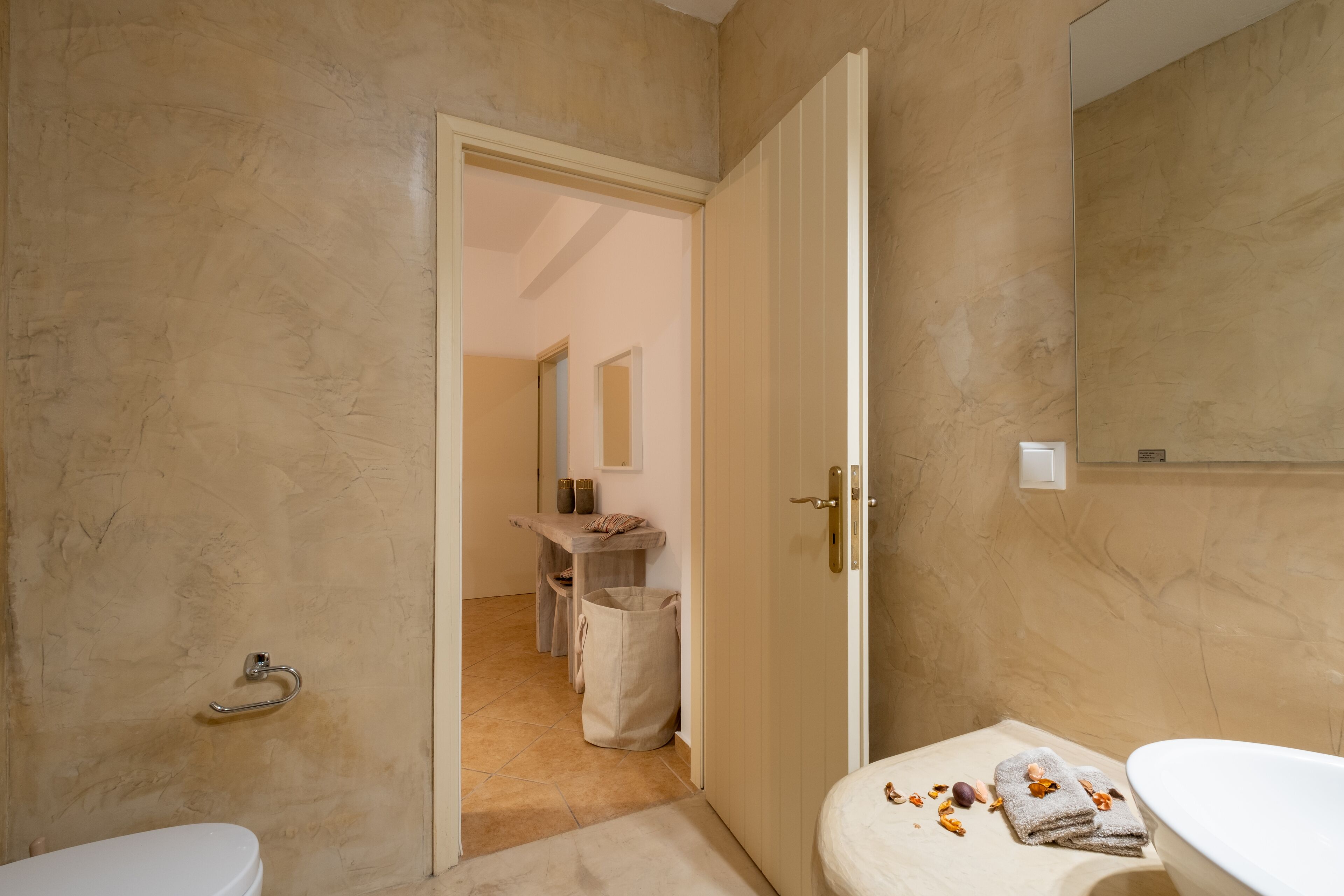 A bathroom with a toilet, a sink, and a mirror. There is a towel on the sink and a bag on the floor.
