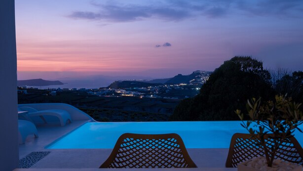 A sunset view from a balcony with a pool, chairs, and a potted plant. - White Orchid Villa (Santorini)
