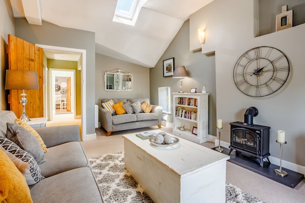 A living room with a grey sofa, a white coffee table, a black wood-burning stove, and a large wall clock.