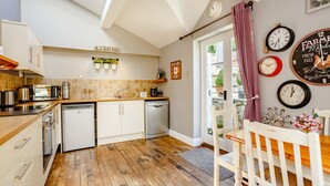 A modern kitchen with wooden flooring, white cabinetry, and a dining area with a wooden table and chairs. - Broadrock (Chepstow)